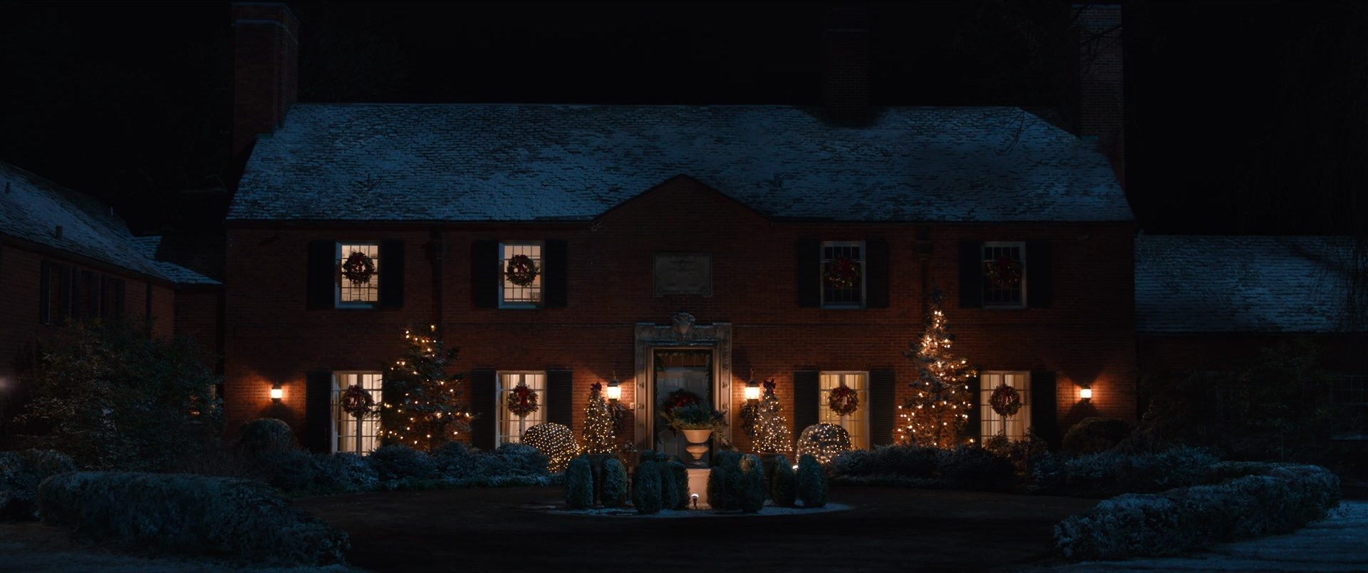 A brick house at night dressed with wreaths and warm windows